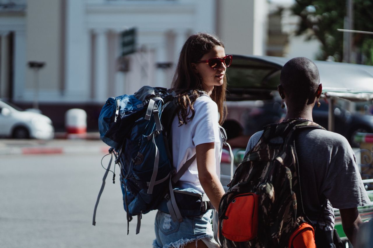Two travelers with backpacks walking in a sunny urban environment.
